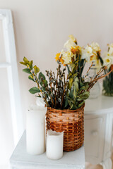 Arrangement of flowers, daffodils, willow, near the bottom of the candle. Against the background of a white room