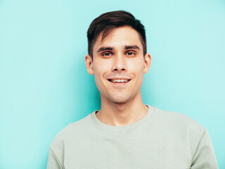 Portrait of handsome smiling stylish hipster lambersexual model.Man dressed in T-shirt and jeans. Fashion male isolated in studio. Posing near blue wall. Cheerful and happy