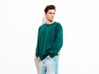 Fototapeta premium Portrait of handsome confident stylish hipster lambersexual model.Man dressed in green sweater and jeans. Fashion male posing in studio near white wall. Isolated