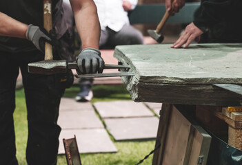 Skilled stonemason splits Slate Rock with a chisel. Shallow depth of field. - obrazy, fototapety, plakaty