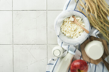 Shavuot jewish holiday celebration. Milk and cheese, ripe wheat and fruits, cream old cracked tile wall background. Dairy products over white wooden background. Shavuot concept. Top view. Mock up.