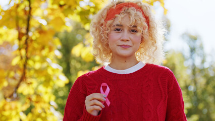 Outdoor shot of a cute young adult European woman with beautiful curly hair in red sweater holding...