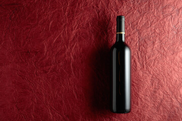 Bottle of red wine on a crumpled red paper background.