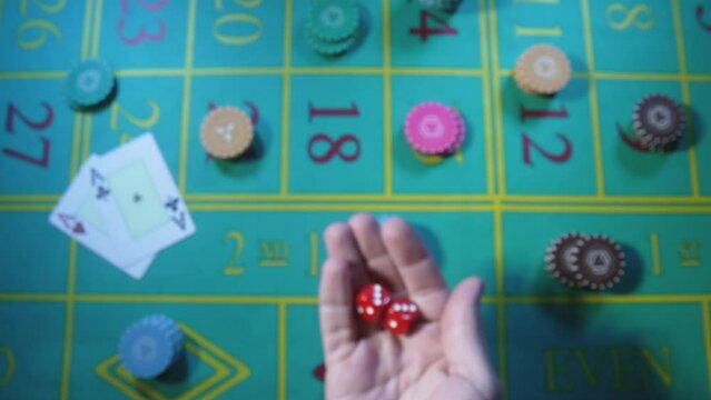 Male hand tossing up red dice in slow motion against background of green roulette table in casino. Man gambler, gambling, craps, poker. Casino chips and cards are laid out on gaming table close up.