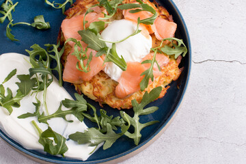 Fried draniki with red salted fish and poached egg. A dish decorated with herbs and sour cream