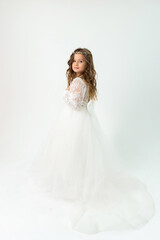 A little girl in a white dress and tiara posing on a white background in the studio