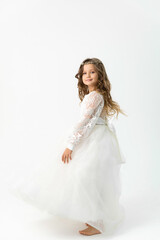 Smiling little girl dancing barefoot in a white dress on a white background in the studio