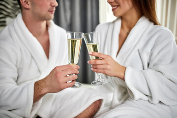 Beauty, spa, healthy lifestyle concept. Beautiful young couple in bathrobes relaxing at luxury hotel room. The boy and the girl are resting in a cozy place and drinking wine. Wellness theme