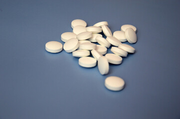 A bunch of prescription pills. White pills are loosely scattered on a blue background. Vitamins, medicine, treatment. Free space for text.
