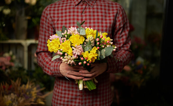 Male in shirt holding beautiful bouquet of yellow and pink fresh spring flowers. Theme of love, dating or romance. Mother's Day, Valentine's Day or International Women Day concept. High quality photo