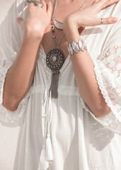 wedding details. close up round silver esoteric jewelry on female neck near hands on the white boho style dress background at sunny day. jewelry concept, free space