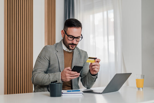Serious businessman making credit card payment through smart phone at workplace