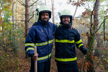 Happy firefighters men after action, stopping fire in forest and looking at camera.