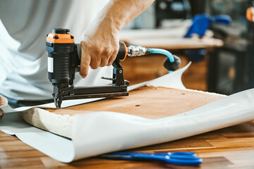 carpenter using  nail gun or staple gun after replace a vinyl or  upholstery fabric to the Seat for...