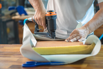 carpenter using  nail gun or staple gun after replace a vinyl or  upholstery fabric to the Seat for Bar Stools,furniture restoration woodworking concept. selective focus