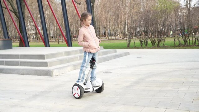 Happy girl standing and spinning on a modern eco-friendly electric self-balancing scooter in a spring park. An electric hoverboard on a city street.