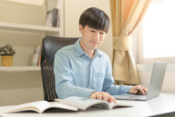 Young Asian college male student writing notes, using laptop for learning online education, business learning, watching online webinar. Businessman is trading, investing on online platform on laptop.