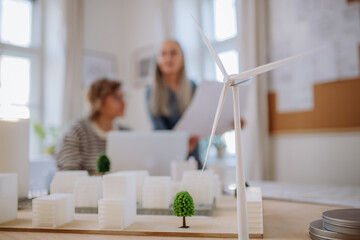Women eco architects working together in office, with wind turbine in foreground.