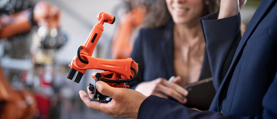 Close-up of man engineer holding model of industrial robotic arm and showing to collegue in factory.