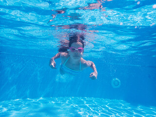 Brave girl with pink goggles is diving in the blue waters of a swimming pool. Sport, recreation, lifestyle concept