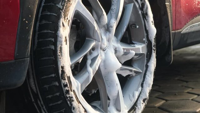 Close-up of a woman's hand washing the alloy wheels of a car with sponge and soap on the car wash. Manual car wash with white soap. Car wash service concept.