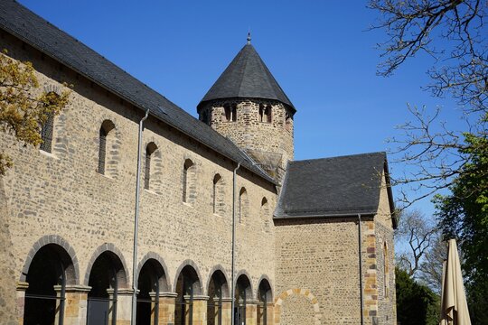 Alte B&auml;ume im Innenhof des Kloster Schiffenberg mit dem Turm der Kapelle und Basilika aus hellem Naturstein vor blauem Himmel im Sonnenschein in Gie&szlig;en an der Lahn in Hessen