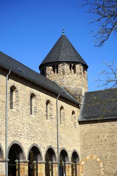 Alte Bäume im Innenhof des Kloster Schiffenberg mit dem Turm der Kapelle und Basilika aus hellem Naturstein vor blauem Himmel im Sonnenschein in Gießen an der Lahn in Hessen