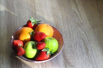 Pink bowl filled with fresh apples, oranges and strawberries on wooden table. Selective focus.