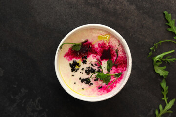 Cauliflower puree potato soup with arugula in round bowl on a black background, top view. Vegetarian healthy food delivery concept	