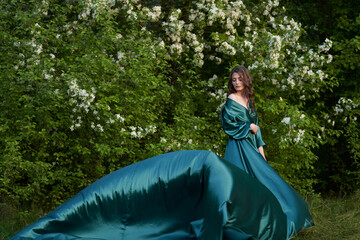 A model in a long silk dress in a blooming apple orchard.