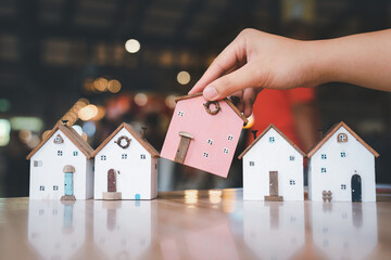 Hand choosing mini wood house model from model on wood table, selective focus, Planning to buy...