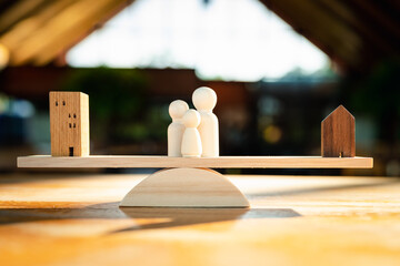 Balanced wood with a model of company building, and a house model with a human figure in the...