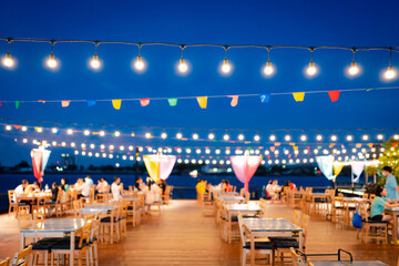Decorative outdoor string lights hanging on electricity post in the garden at night time with blur people. Christmas, festival, holiday and wedding concepts.	