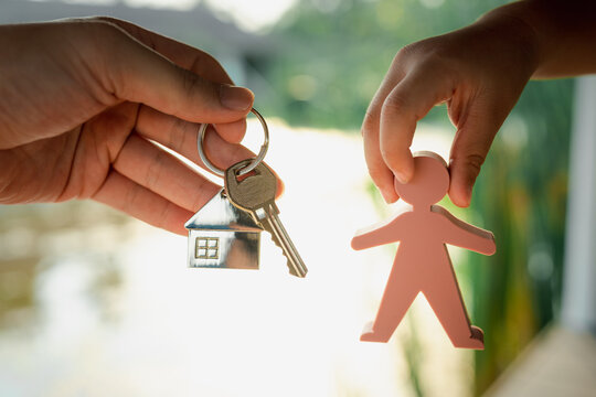 Child Holding A Model Of A Person. Picking Up House Keys And House Keyring From Dad. Concept Of Inheritance And Management