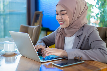 An Asian Muslim businesswoman in a hijab works in 5G online trading on a laptop in her office.