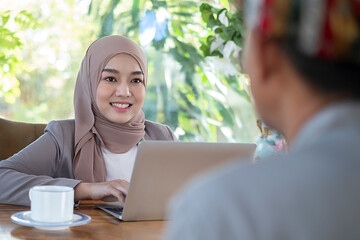 Business concept of signing the joint contract. Beautiful muslim business lady in white hijab sitting together with her bearded african business partner and signing the contract in the office room