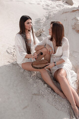 shaman feminine energy. two brunette girls in white boho style dresses are burning a wooden aroma stick and smiling cute on a sand career background in desert at sunny day. lifestyle concept © NASTYA PALEHINA