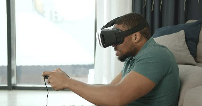 Black man in virtual reality glasses sitting on the carpet