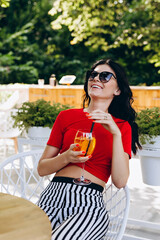 Beautiful smiling brunette with a cocktail in her hands enjoys a moment of relaxation in a cafe