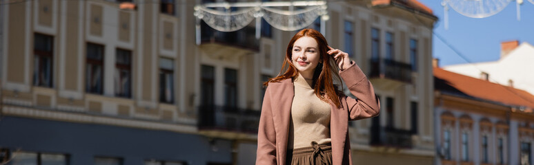 happy redhead woman in coat on street of european city, banner.