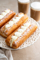 Donut or eclairs and coffee cups with whipped milk, on warm neutral background. Breakfast time.
