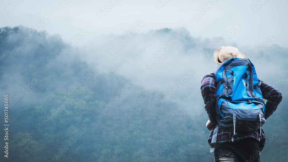 Wall mural African traveler man climbing standing and looking to mountain with misty foggy landscape