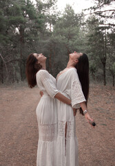 Fototapeta premium female energy party practice. two brunette girls in white boho dresses stand close like mystic witches with smoky burning stick in hand and makes shaman ritual on forest background. lifestyle concept