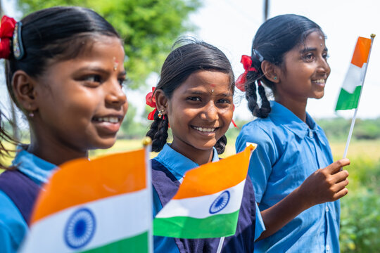 close up of girl kid in school uniform looking at camera while holding indian flag at school - concept of freedom, patriotism and education.