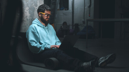 Male IT developer working with software and website at night on a laptop during the war in a dark...