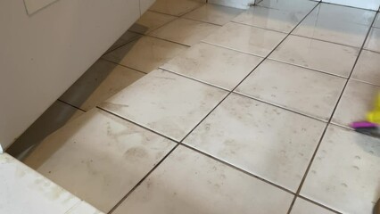 Clean bathroom floor white ceramic tile brushing wet dirty filthy floor stain scrubbing dirt mold by hand wearing yellow rubber protective gloves 