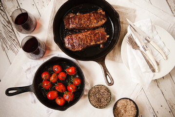 Cast iron pans with strip steaks and tomatoes with red wine