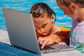 Close up portrait of two cute young girls learning remotely with laptop in swimming pool. Summer holiday and education concept. Selective focus on eyes of one of girls.