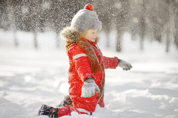 Little boy in red winter clothes having fun with snow. Active outdoors leisure with children in...