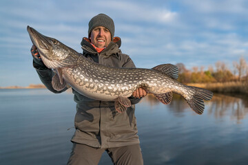 Success pike fishing. Happy fisherman hold huge muskie fish